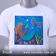 Футболка русалка читає, біла, з верхнього ракурсу, на фоні світло-сірого, принт з русалкою, яка читає книгу, деталі принта яскраві, з акцентами на водоростях та морських елементах, прикріплена етикетка.