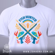 Футболка рибалка мисливець, біла, зображена зверху, фон світло-сірий, принт з рибами, гарпунами та рослинами, прикріплена етикетка з зеленим шнурком.