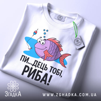 Футболка рибальський настрій. Біла футболка, складена вдвічі, з принтом риби, що має великі очі і усмішку, поряд з поплавком. Текст чорного кольору: 'ПИ...ДЕЦЬ ТОБІ, РИБА!'. На футболці є етикетка з зеленим шнурком. Фон світлий, з легким відблиском.