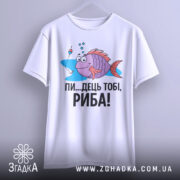 Футболка рибальський настрій. Біла футболка, підвішена на вішалці, з принтом риби, що усміхається, на фоні світло-сірого кольору. Принт яскравий, з текстом чорного кольору: 'ПИ...ДЕЦЬ ТОБІ, РИБА!'. Футболка виглядає стильно і сучасно.