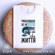 Футболка риболовля це життя. Біла футболка, що лежить на плетеній кошику. Ракурс зверху, фон натуральний, принт з рибою та текстом яскраво контрастує.