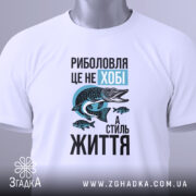 Футболка риболовля це життя. Біла футболка, що лежить на поверхні, з видимим ярликом. Ракурс зверху, фон світлий, принт з рибою та текстом яскравий.