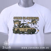 Футболка сафарі на окупанта, білого кольору, складена на столі, фон світло-сірий, принт з військовим, що стріляє з автомобіля, з українським прапором, на етикетці зелена стрічка.
