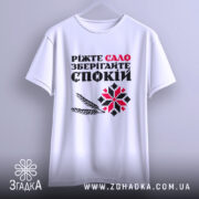 Футболка сало і спокій, біла футболка підвішена на вішалці, фон світло-сірий, принт з текстом "Ріжте сало зберігайте спокій" у червоному та чорному кольорах, з графічними елементами у вигляді колосків і візерунка.