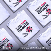 Футболка сало і спокій, біла футболка на манекені, фон світло-сірий, принт містить текст "Ріжте сало зберігайте спокій" з червоними та чорними літерами, а також графічні елементи у вигляді колосків і візерунка.