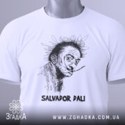 Футболка Сальвадор Далі білого кольору, зображена зверху, на ній підвішений ярлик з зеленим шнурком, фон світло-сірий, принт з портретом Сальвадора Далі в чорному кольорі, підпис 'SALVADOR DALI' внизу.
