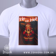 Футболка Санта білого кольору, складена на столі, фон світло-сірий, принт з Сантою в червоному костюмі, який вигукує 'Ho Ho Ho!', з етикеткою на зеленому шнурку.