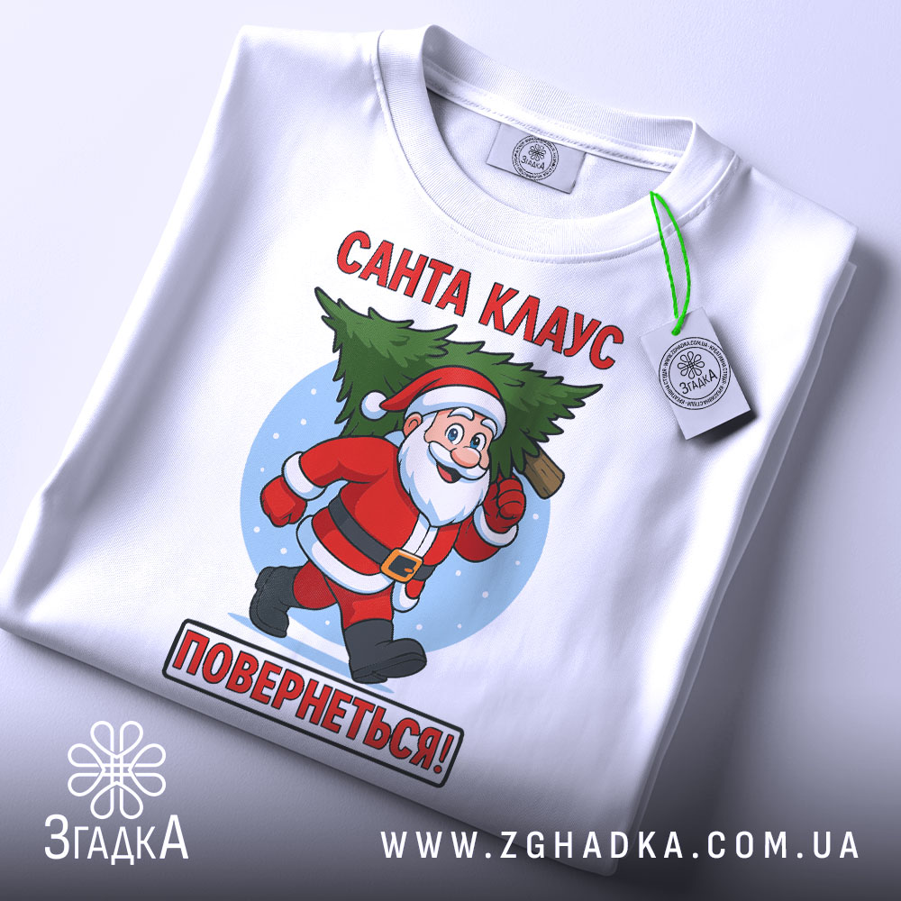 Футболка Санта Клаус повернеться, біла, зображена з верхнього ракурсу, фон світлий, принт з Санта Клаусом, який біжить з ялинкою, текст червоним кольором: 'Санта КЛАУС ПОВЕРНЕТЬСЯ!', на футболці є етикетка з зеленим шнурком.