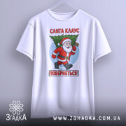 Футболка Санта Клаус повернеться, біла, зображена з фронтального ракурсу, фон світлий, принт з Санта Клаусом, який біжить з ялинкою, текст червоним кольором: 'Санта КЛАУС ПОВЕРНЕТЬСЯ!', футболка висить на вішалці.