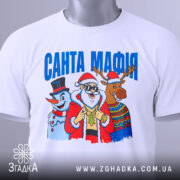 Футболка Санта Мафія білого кольору, складена на поверхні, ракурс зверху, фон світло-сірий, принт з Сантою, сніговиком і оленем, текст "САНТА МАФІЯ" вгорі, на футболці є етикетка.