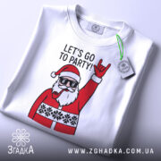 Футболка Санта рок, біла, складена на столі, фон світло-сірий, принт з Сантою в окулярах, який піднімає руку в жесті рокера, текст "LET'S GO TO PARTY!" над принтом, на футболці є етикетка.