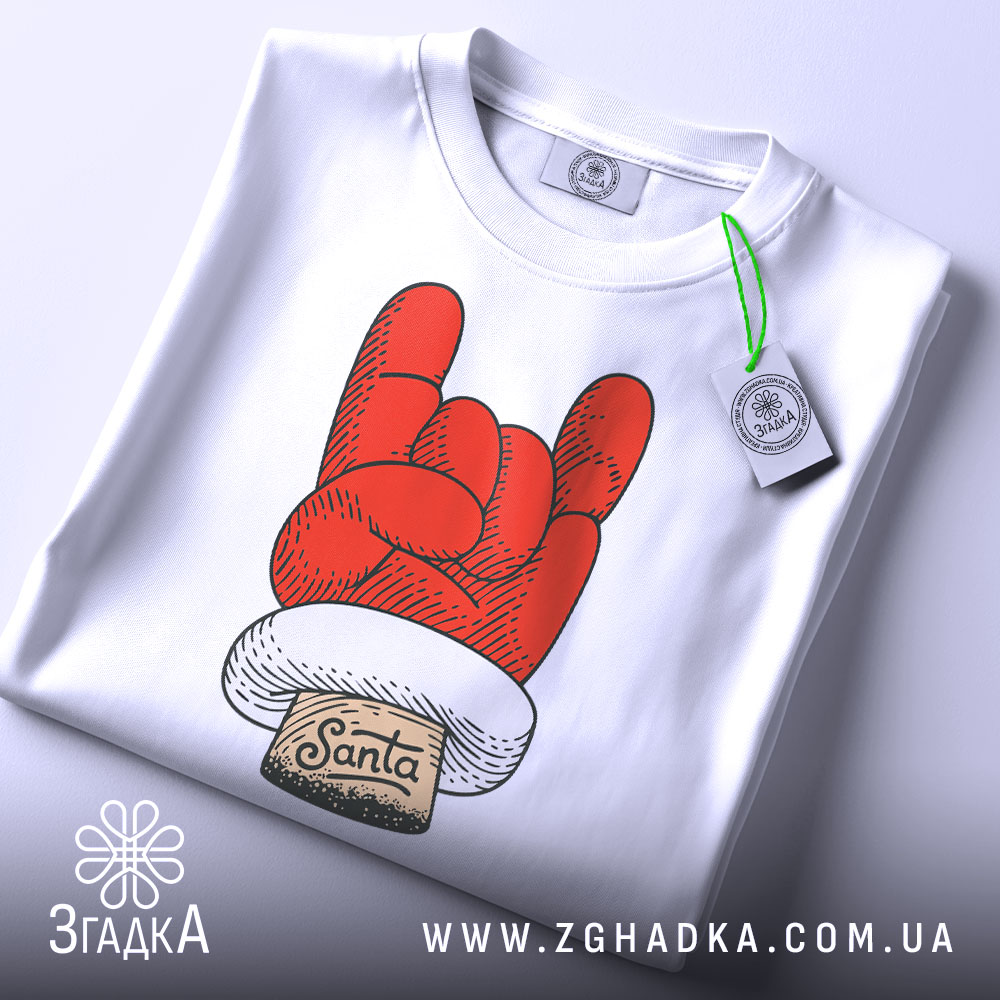 Футболка Санта рок, біла, зображена зверху, на фоні світло-сірого кольору, принт червоного кольору у формі руки з жестом рок, з написом 'Santa' на етикетці, з зеленим ярликом.