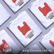 Футболка Санта рок, біла, зображена з фронтального ракурсу, на фоні світло-сірого кольору, принт червоного кольору у формі руки з жестом рок, з написом 'Santa' на етикетці.