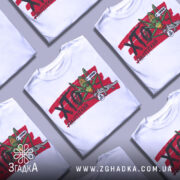 Футболка сарана, біла, зображена на манекені, фон світло-сірий, принт з зеленим саранчою та сірим ящіркою на червоному фоні з написом "ХТО?".