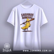 Футболка Savannah Bananas білого кольору, підвішена на вішалці, фон світло-сірий, принт з жовтою бананою в окулярах та битою, текст 'SAVANNAH BANANAS' над малюнком.