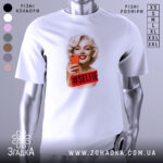 Футболка селфі Мерилін, біла, зображена на манекені, фон світло-сірий, принт з усміхненою Мерилін Монро, яка тримає червоний телефон, з написом #SELFIE на червоному фоні.