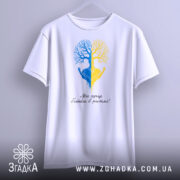 Футболка серце в ритмі, біла, підвішена на вішалці, фон світло-сірий, принт з двох дерев, одне синє, інше жовте, з руками, що тримають серце, під написом 'Моє серце б'ється в ритмі!'.