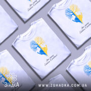 Футболка серце в ритмі, біла, зображена на манекені, фон світло-сірий, принт з двох дерев, одне синє, інше жовте, з руками, що тримають серце, під написом 'Моє серце б'ється в ритмі!'