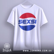 Футболка SEXSI білого кольору, підвішена на вішалці, з великим принтом у вигляді червоного та синього кола, на якому написано 'SEXSI' великими літерами, фон світло-сірий, футболка має вільний крій.