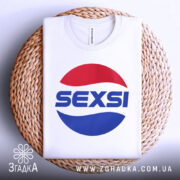 Футболка SEXSI білого кольору, складена на плетеній кошику, з великим принтом у вигляді червоного та синього кола, на якому написано 'SEXSI' великими літерами, фон світло-сірий, видно етикетку з написом 'zgadka.com.ua'.