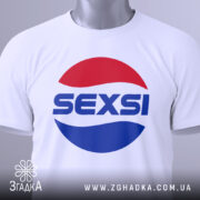 Футболка SEXSI білого кольору, складена на поверхні, з великим принтом у вигляді червоного та синього кола, на якому написано 'SEXSI' великими літерами, на фоні світло-сірого кольору, з видимою етикеткою з зеленим шнурком.