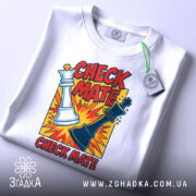 Футболка шах і мат, біла, зображена з верхнього ракурсу, на фоні світло-сірого кольору, принт з шаховими фігурами та текстом 'CHECK MATE', з етикеткою на шнурку.