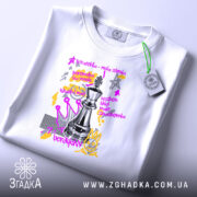 Футболка шахова стратегія, біла, зображена на столі, фон світлий, принт з шаховою фігурою та текстом, прикріплена етикетка з логотипом.