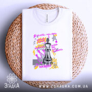 Футболка шахова стратегія, біла, розкладена на плетеній основі, фон нейтральний, принт з шаховою фігурою та кольоровими графічними елементами, текст на принті в жовтому та фіолетовому кольорах.