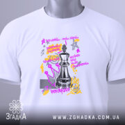 Футболка шахова стратегія, біла, зображена на столі, фон світлий, принт з шаховою фігурою та текстом, прикріплена етикетка з логотипом.