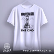 Футболка шаховий король, біла, підвішена на вішалці, фон світло-сірий, принт з шаховою фігурою короля та текстом 'GAMBLER THE KING' у чорному кольорі.