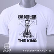 Футболка шаховий король, біла, зображена в горизонтальному положенні, фон світло-сірий, принт з шаховою фігурою короля та текстом 'GAMBLER THE KING', на футболці є етикетка з зеленим шнурком.