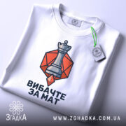 Футболка шаховий король, біла, зображена зверху, фон світлий, принт з шаховою фігурою короля на оранжевому фоні, з етикеткою, що звисає.