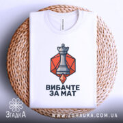 Футболка шаховий король, біла, зображена зверху, фон світлий, принт з шаховою фігурою короля на оранжевому фоні, розташована на плетеній основі.