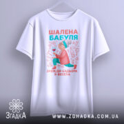 Футболка шалена бабуля, білого кольору, підвішена на вішалці, фон світло-сірий, принт з бабусею, що тримає келих, в яскравих кольорах.