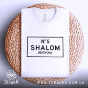 Футболка шалом Бердичів, біла, зображена зверху на плетеній кошику, фон світлий, принт чорного кольору з написом 'N°5 SHALOM BERDYCHIV' у прямокутній рамці.