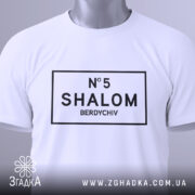 Футболка шалом Бердичів, біла, зображена зверху, на ній видно етикетку з зеленим шнурком, принт чорного кольору з написом 'N°5 SHALOM BERDYCHIV' у прямокутній рамці.