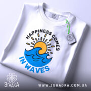 Футболка щастя у хвилях, біла, зображена зверху, складена, фон світлий, на футболці принт з сонцем і хвилями, з етикеткою на зеленому шнурку.