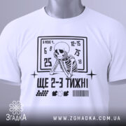 Футболка ще 2-3 тижні, біла, складена на поверхні, фон світло-сірий, принт з чорним скелетом, що сидить, та текстом, на ярлику зелена стрічка.