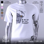 Футболка що це ви робите. Біла футболка з принтом птаха, який виглядає з-за стіни, з текстом 'А що це Ви тут Робите?'. Зображення з фронтального ракурсу, фон світлий.