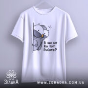 Футболка що це ви робите. Біла футболка на вішалці, з принтом птаха, який виглядає з-за стіни, з текстом 'А що це Ви тут Робите?'. Вид з фронтального ракурсу, фон світлий.