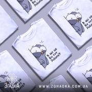 Футболка що це ви робите. Біла футболка з принтом птаха, який виглядає з-за стіни, з текстом 'А що це Ви тут Робите?'. Зображення з фронтального ракурсу, фон світлий.