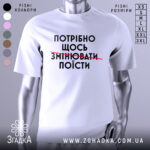 Футболка білого кольору, зображена з фронтального ракурсу на манекені, фон світло-сірий, принт чорного кольору з текстом "ПОТРІБНО ЩОСЬ ЗМІНЮВАТИ ПОЇСТИ".
