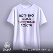 Футболка білого кольору, зображена з фронтального ракурсу, фон світло-сірий, принт чорного кольору з текстом "ПОТРІБНО ЩОСЬ ЗМІНЮВАТИ ПОЇСТИ".