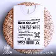 Футболка шеф бариста білого кольору, складена на плетеній основі, фон натуральний, принт з текстом і графікою, напис '100% ECO'.