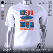 Футболка Shelby GT білого кольору, зображена на манекені, ракурс спереду, фон світло-сірий, принт містить зображення автомобіля Shelby GT500 та текст "500 SHELBY" в червоному та синьому кольорах.