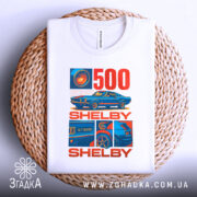 Футболка Shelby GT білого кольору, зображена на плетеній основі, ракурс зверху, фон білий, принт містить зображення автомобіля Shelby GT500 та текст "500 SHELBY" в червоному та синьому кольорах.