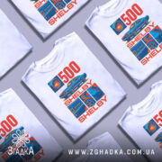 Футболка Shelby GT білого кольору, зображена на манекені, ракурс спереду, фон світло-сірий, принт містить зображення автомобіля Shelby GT500 та текст "500 SHELBY" в червоному та синьому кольорах.