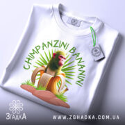 Футболка Shimpanzini Bananini білого кольору, зображена з верхнього ракурсу, на ній видно принт з мавпою на банані, фон світло-сірий, на футболці є етикетка.
