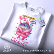 Футболка шубка жопку гріла, біла, зображена зверху, фон світло-сірий, принт з рибою в рожевій шубі та окулярах, на футболці є етикетка.