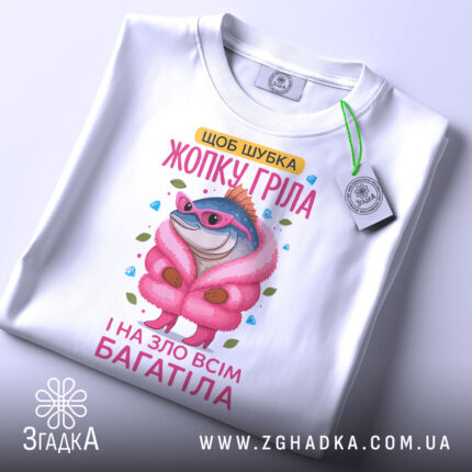 Футболка шубка жопку гріла, біла, зображена зверху, фон світло-сірий, принт з рибою в рожевій шубі та окулярах, на футболці є етикетка.